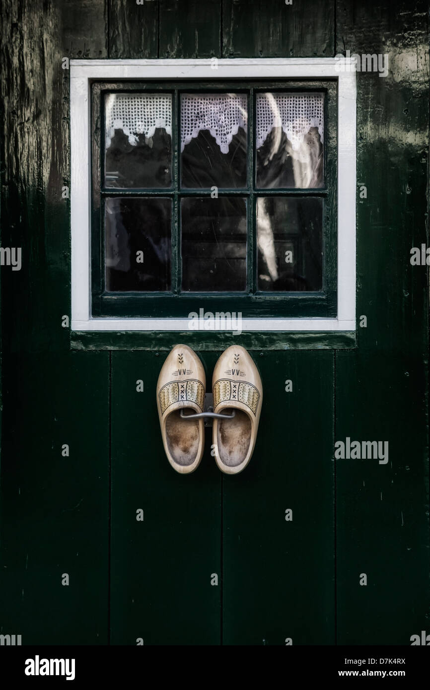 Dutch zapatos de madera colgando de una puerta verde con una ventana. Foto de stock