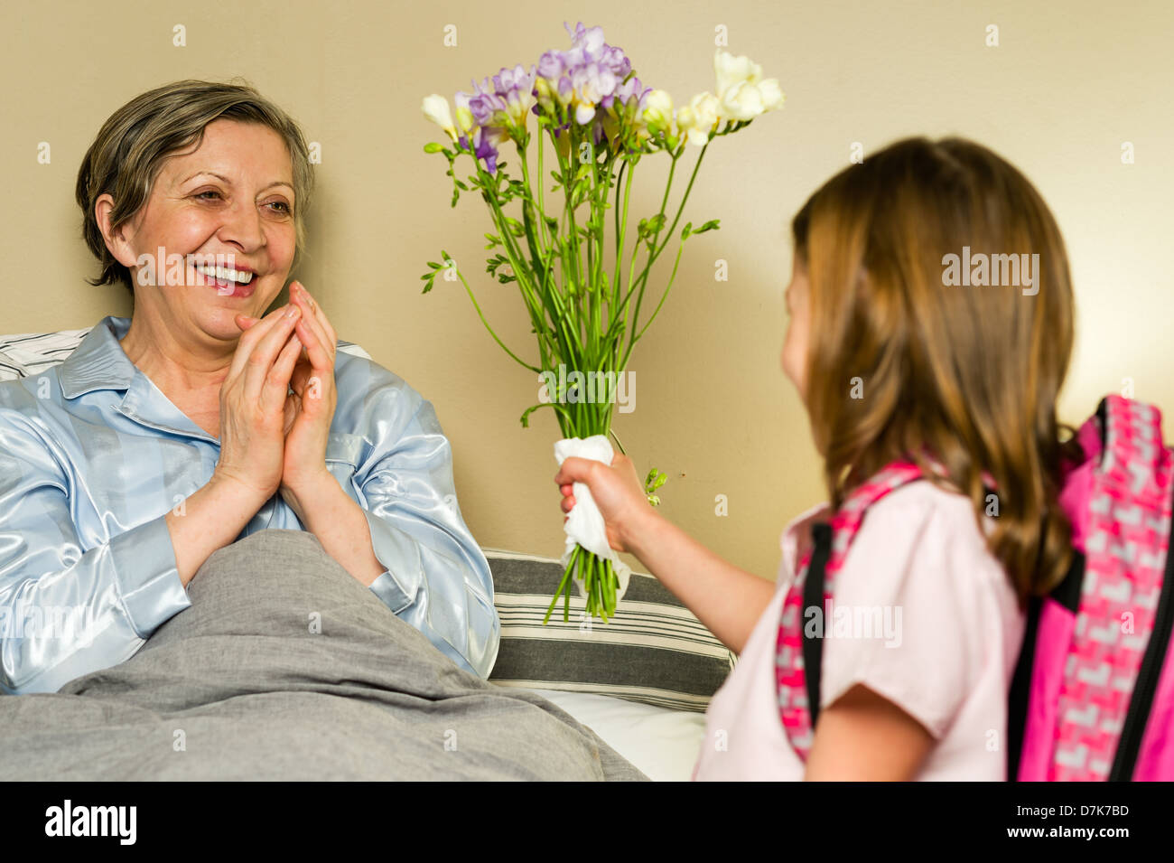 Nieto dando ramo de flores a la abuela acostado en la cama Foto de stock