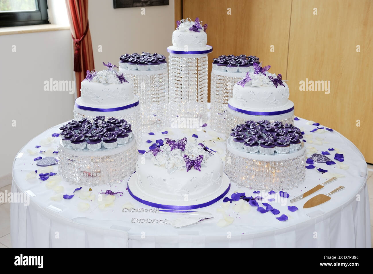 Gran boda blanco y morado pastel de boda en la recepción decorada con pétalos y mariposas Foto de stock