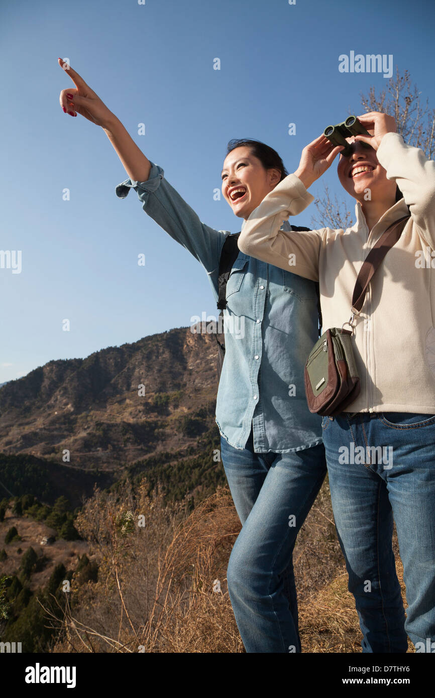 Las mujeres senderismo, utilizando binoculares, apuntando a la cima de la montaña Foto de stock