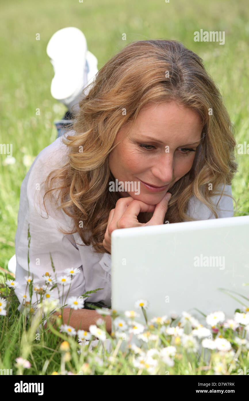 Mujer relajado acostado en un campo de margaritas utilizando su ordenador portátil Foto de stock