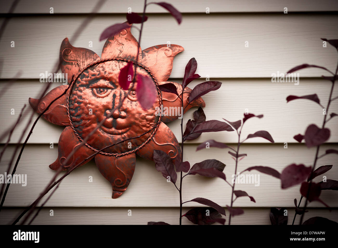 Un sonriente sol rostro ornamento metálico colgado en una pared. Foto de stock