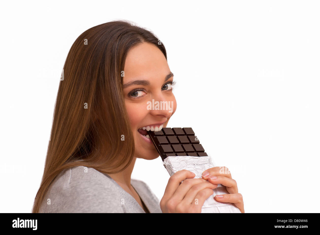 Retrato de joven bella morder una barra de chocolate. Fondo blanco. Mirando a la cámara Foto de stock