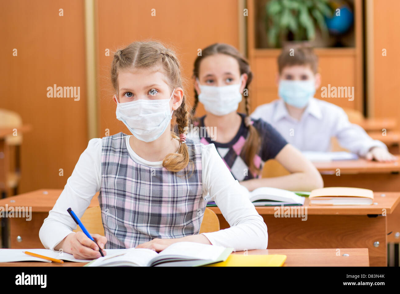 Schoolkids con máscara de protección contra el virus de la gripe en la lección Foto de stock