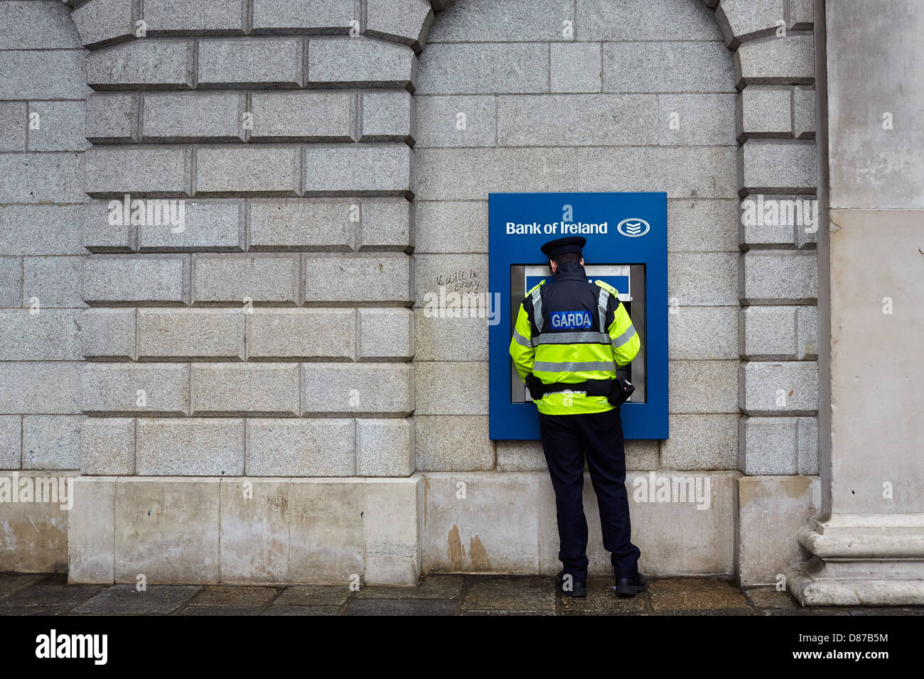 Miembro de la Garda (policía irlandesa) usando un cajero automático en el banco de Irlanda durante una recesión. College Green, Dublín, Irlanda Foto de stock