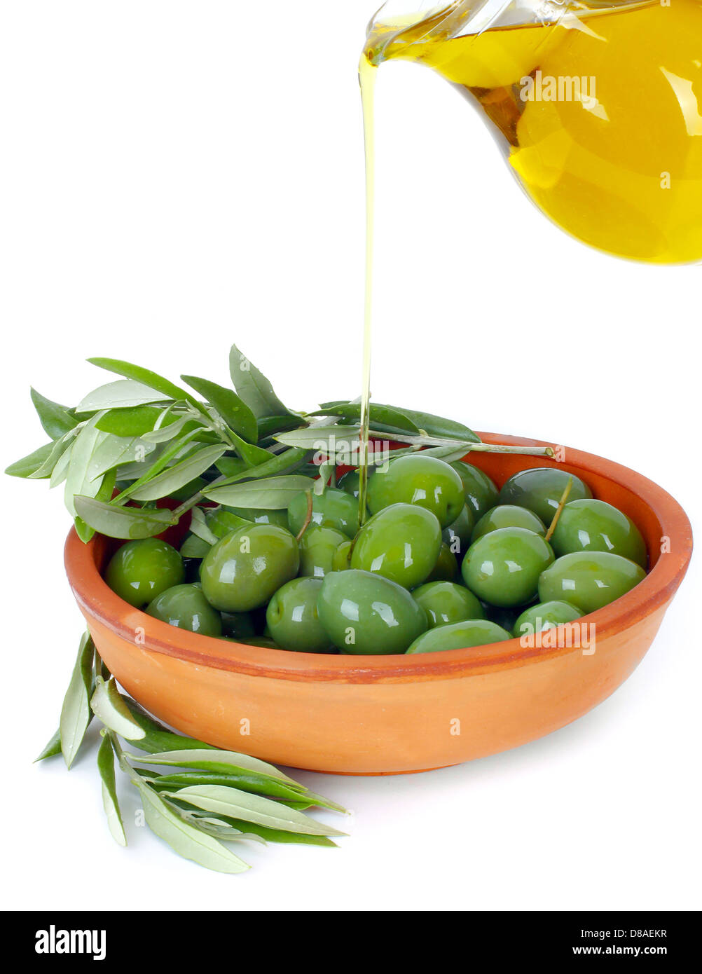 El aceite de oliva que fluyen de una jarra en un recipiente de terracota con las ramas de un árbol de oliva Foto de stock