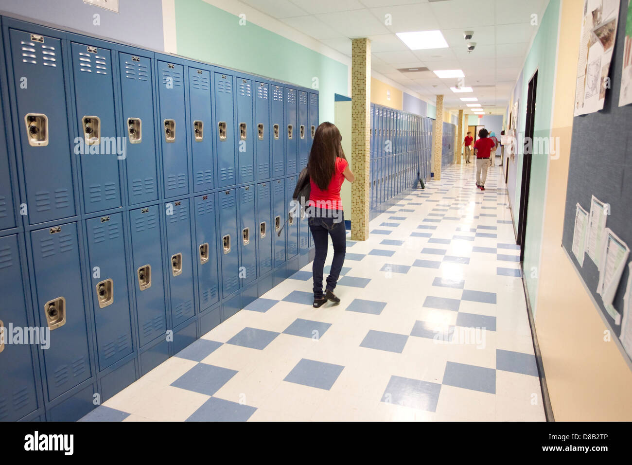 Estudiante de la escuela secundaria femenina llevando una mochila, camina por el pasillo con armarios en Austin, Texas School Foto de stock