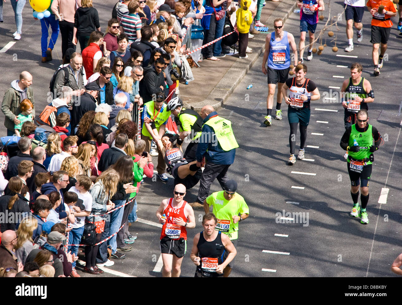 Runner siendo llevado por funcionarios tras la contracción durante 2013 maratón de Londres Victoria Embankment Inglaterra Europa Foto de stock
