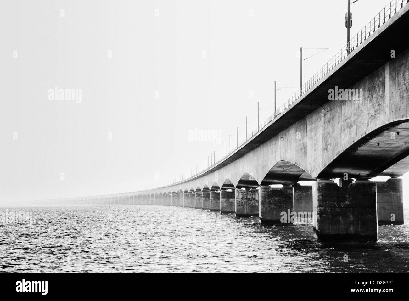 Imagen en blanco y negro del histórico puente curvándose por sobre el agua y desaparecer en la niebla costera en Nyborg, Dinamarca Foto de stock