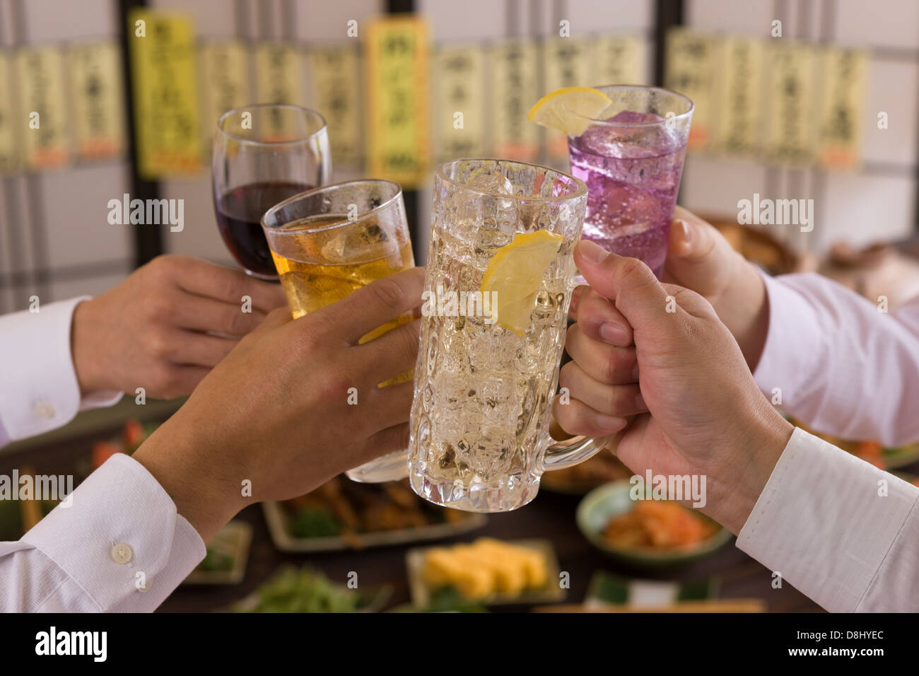Cuatro personas brindando con unos a otros con diversas bebidas en Izakaya Foto de stock