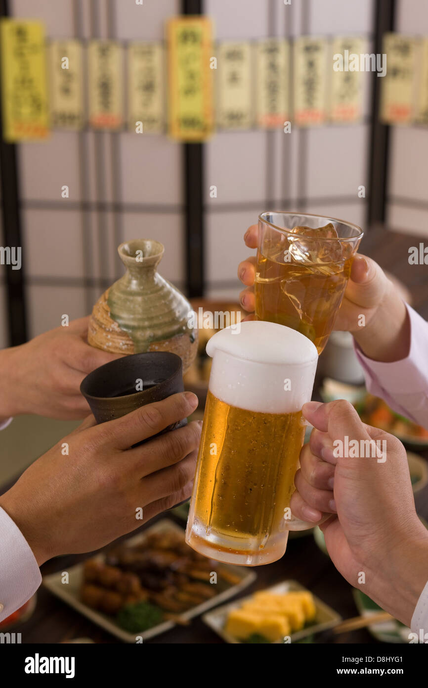Cuatro personas brindando con unos a otros con diversas bebidas en Izakaya Foto de stock