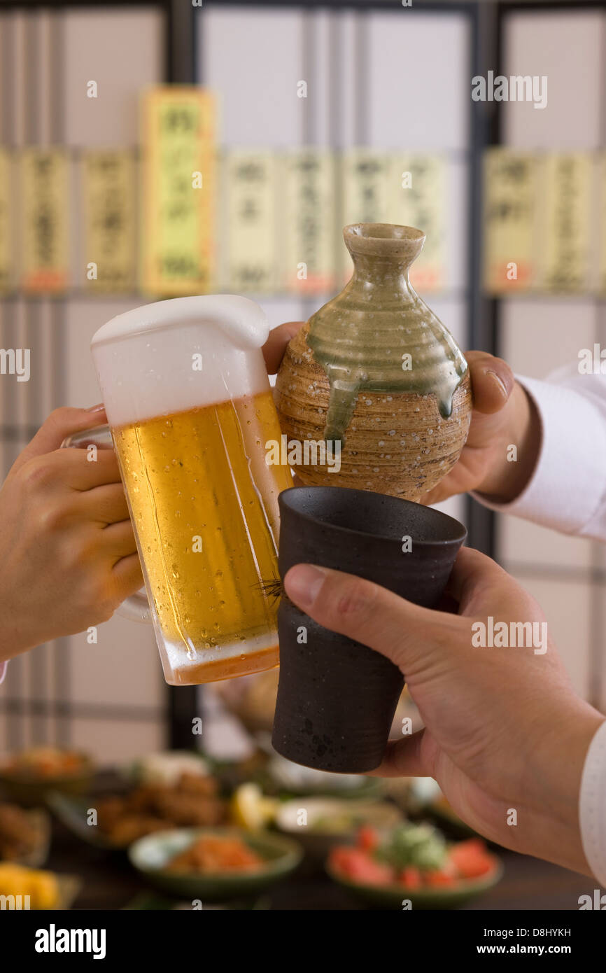 Tres personas tostar unas con otras y con diversas bebidas en Izakaya Foto de stock