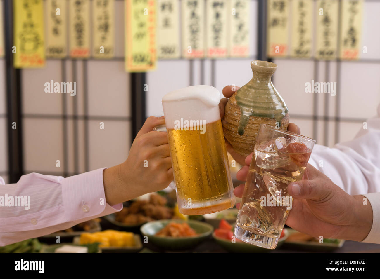 Tres personas tostar unas con otras y con diversas bebidas en Izakaya Foto de stock