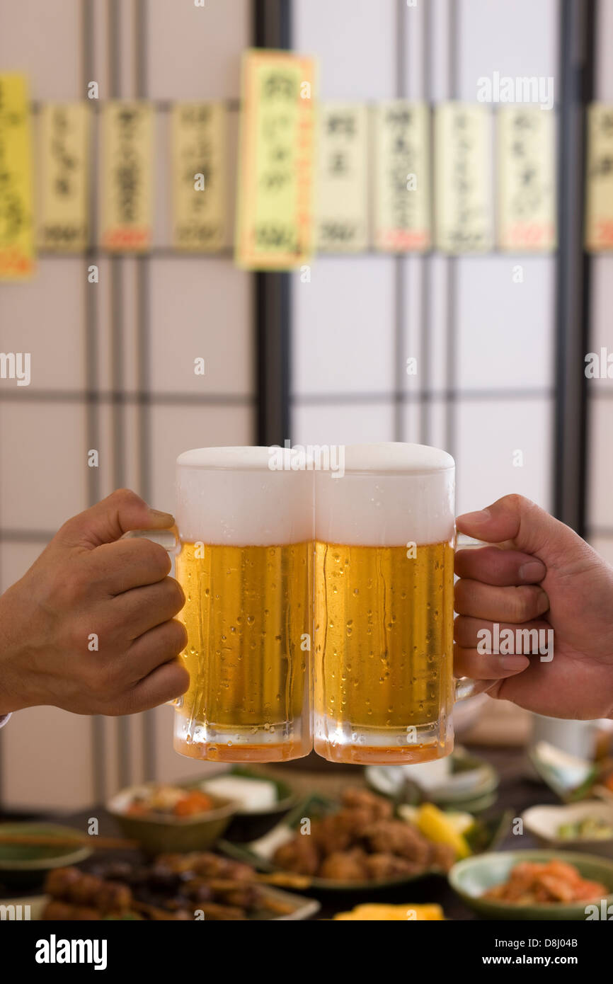 Dos personas brindando con cerveza en Izakaya Foto de stock