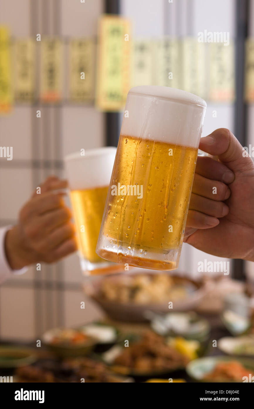 Dos personas brindando con cerveza en Izakaya Foto de stock