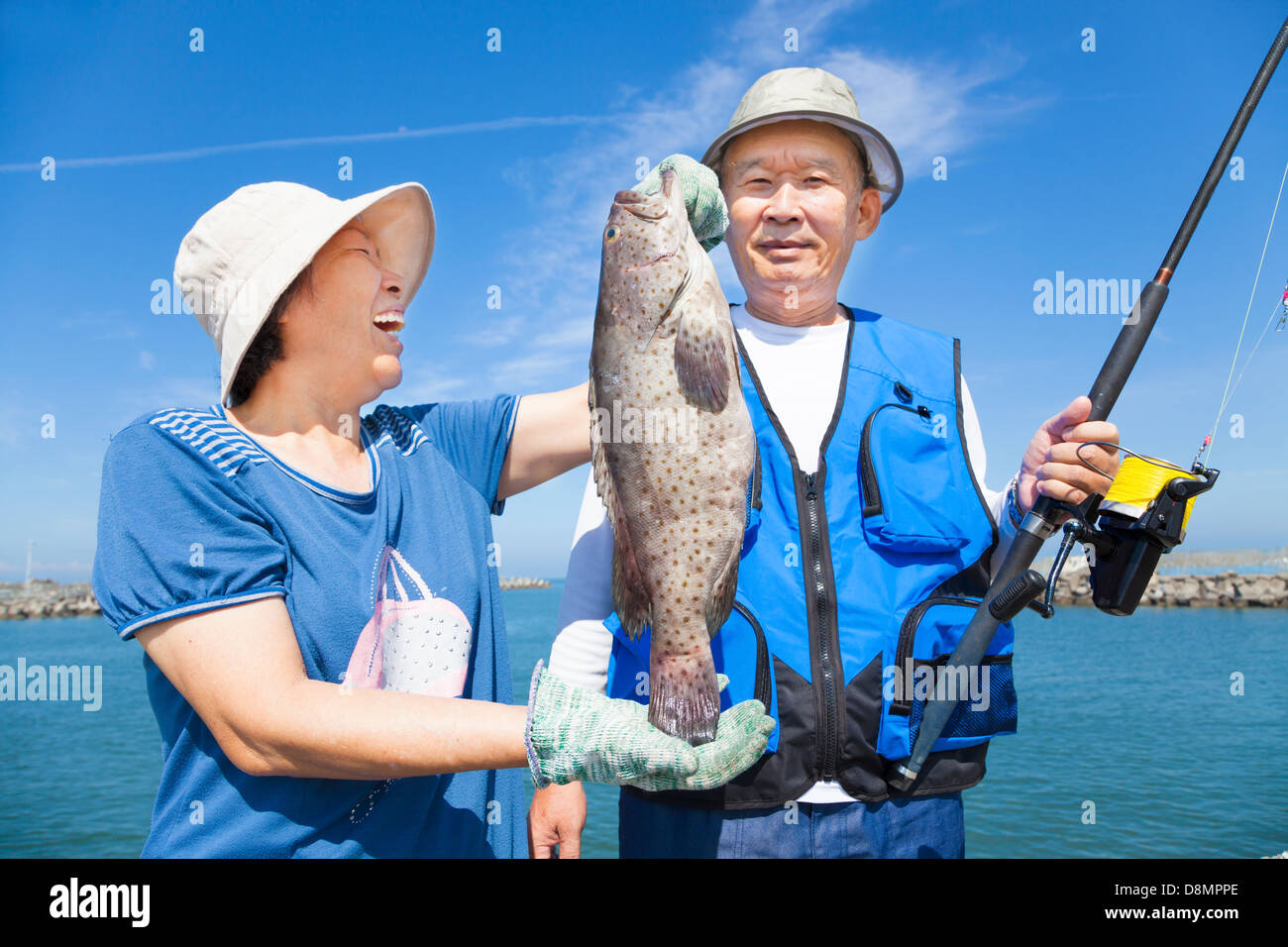 Feliz pareja senior de Asia la pesca y mostrando gran agrupador Foto de stock