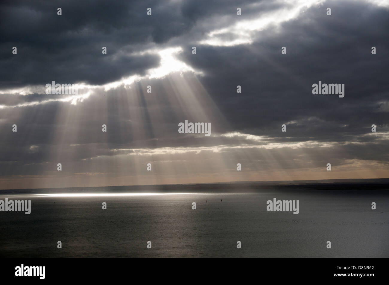 Los haces de luz a través de nubes de tormenta en la costa del mar, con vista al mar en calma Foto de stock