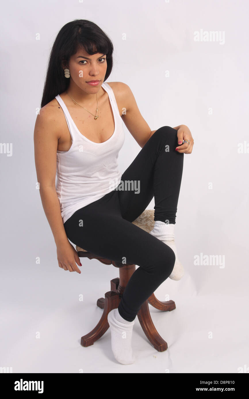 Hermosa, joven, de pelo negro latino en una camiseta blanca con una bonita sonrisa, sentado en el pequeño taburete. Foto de stock