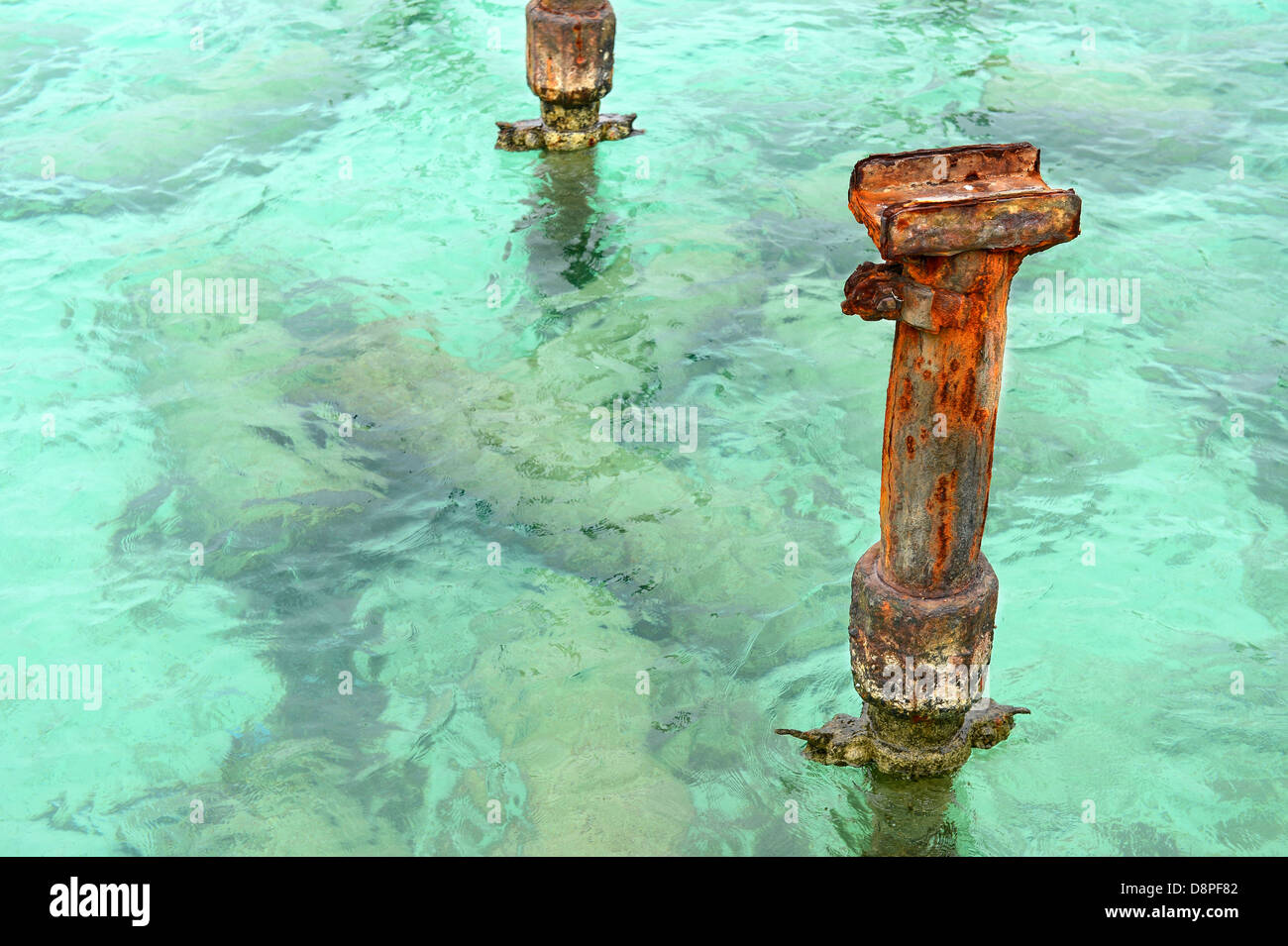 Rusted metal puestos desde el muelle en aguas del Caribe claras Foto de stock