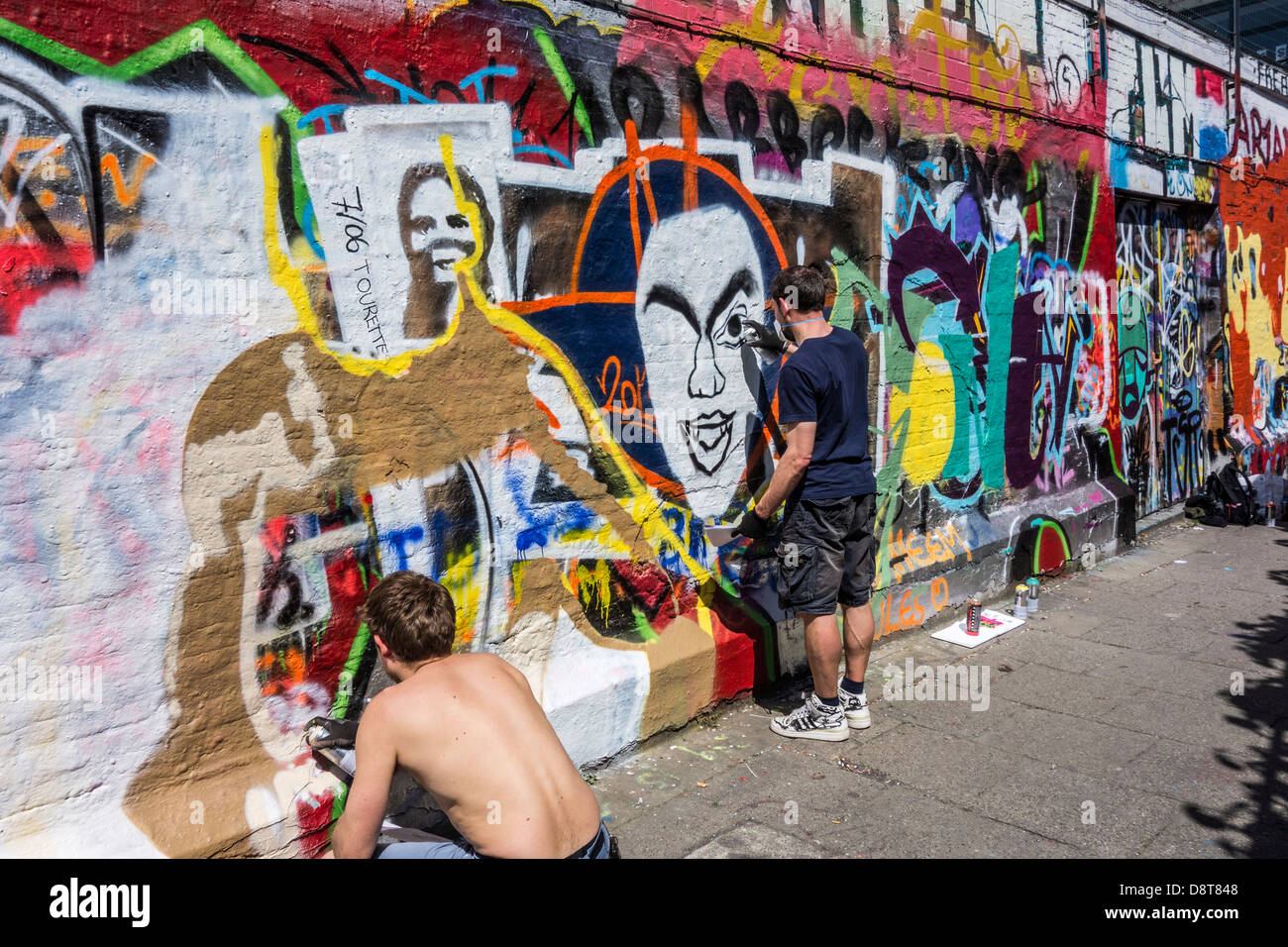 Jóvenes con botes de spray de pulverización callejón colorido graffiti en la pared del edificio en la ciudad Foto de stock