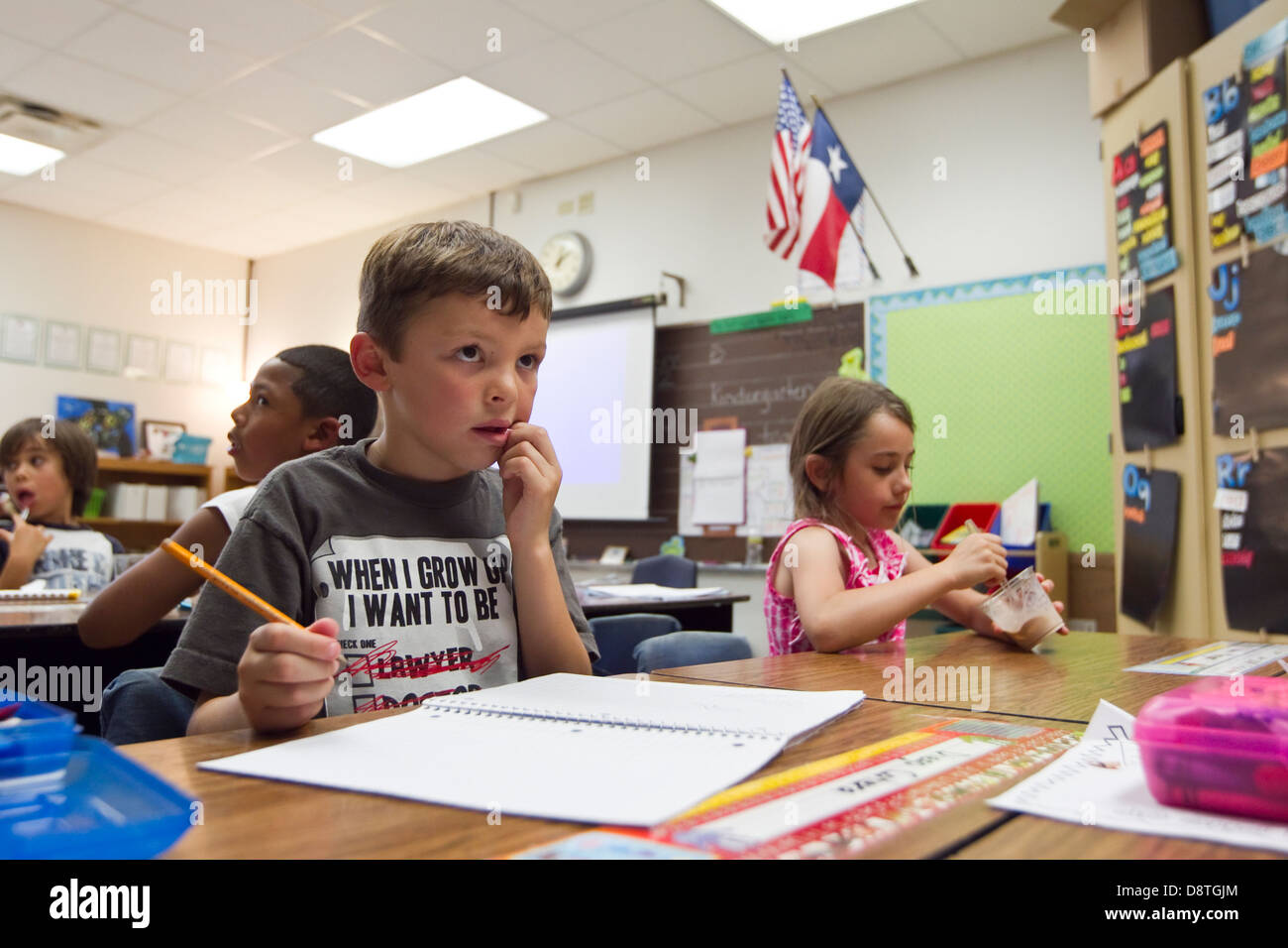 7 años chico mexicano-americana se asienta en las aulas de la escuela elemental de primer grado y escribe en el bloc de notas con un lápiz Foto de stock