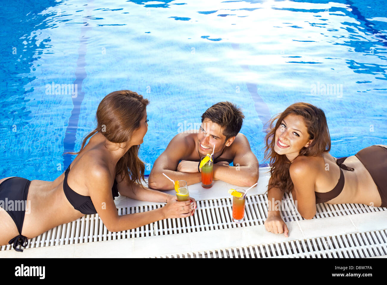 Apuesto de en una piscina azul brillante charlando con dos hermosas mujeres bikini tomando el sol en el borde Fotografía de stock -