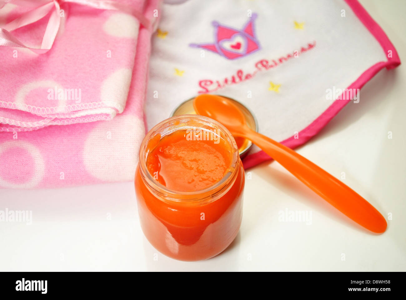 La comida del bebé naranja con un babero rosa y blanco Foto de stock