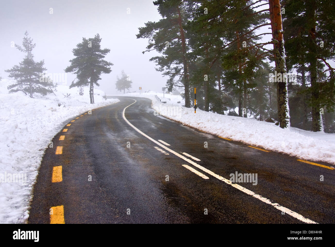 Paisaje nevado de una carretera de montaña con pistas en amarillo y blanco. Foto de stock