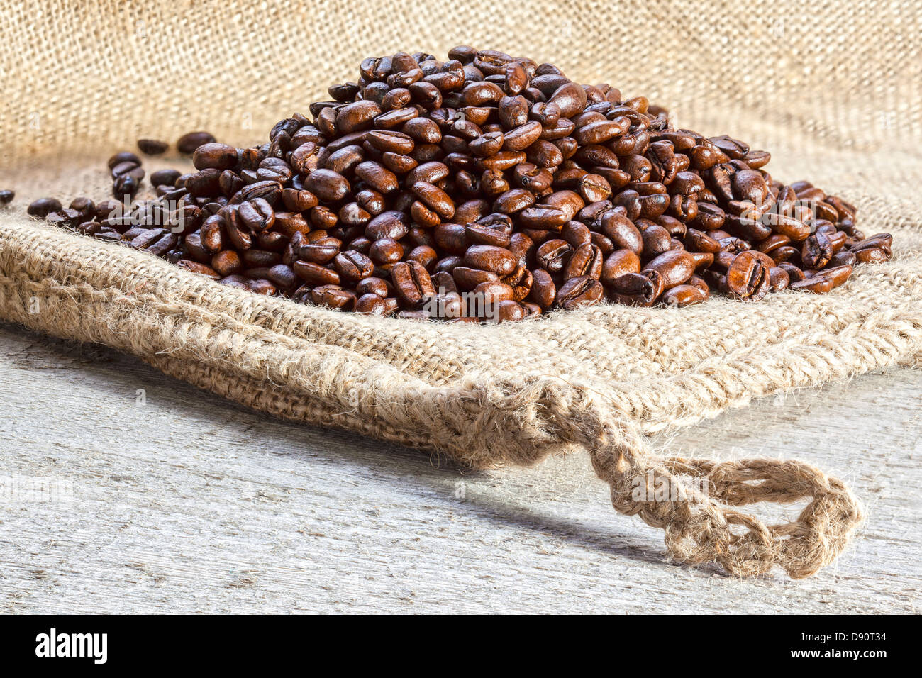 Los granos de café en sacos de arpillera - montones de café tostado en grano en un saco de yute o arpillera. Foto de stock