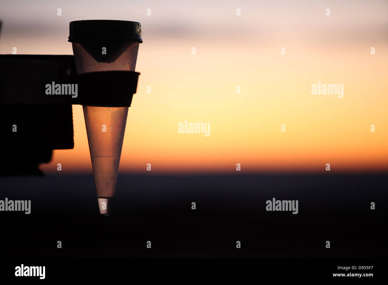 Foto de una silueta de un medidor de lluvia o medidor de lluvia tomadas al amanecer con colores dorados en el fondo. Foto de stock