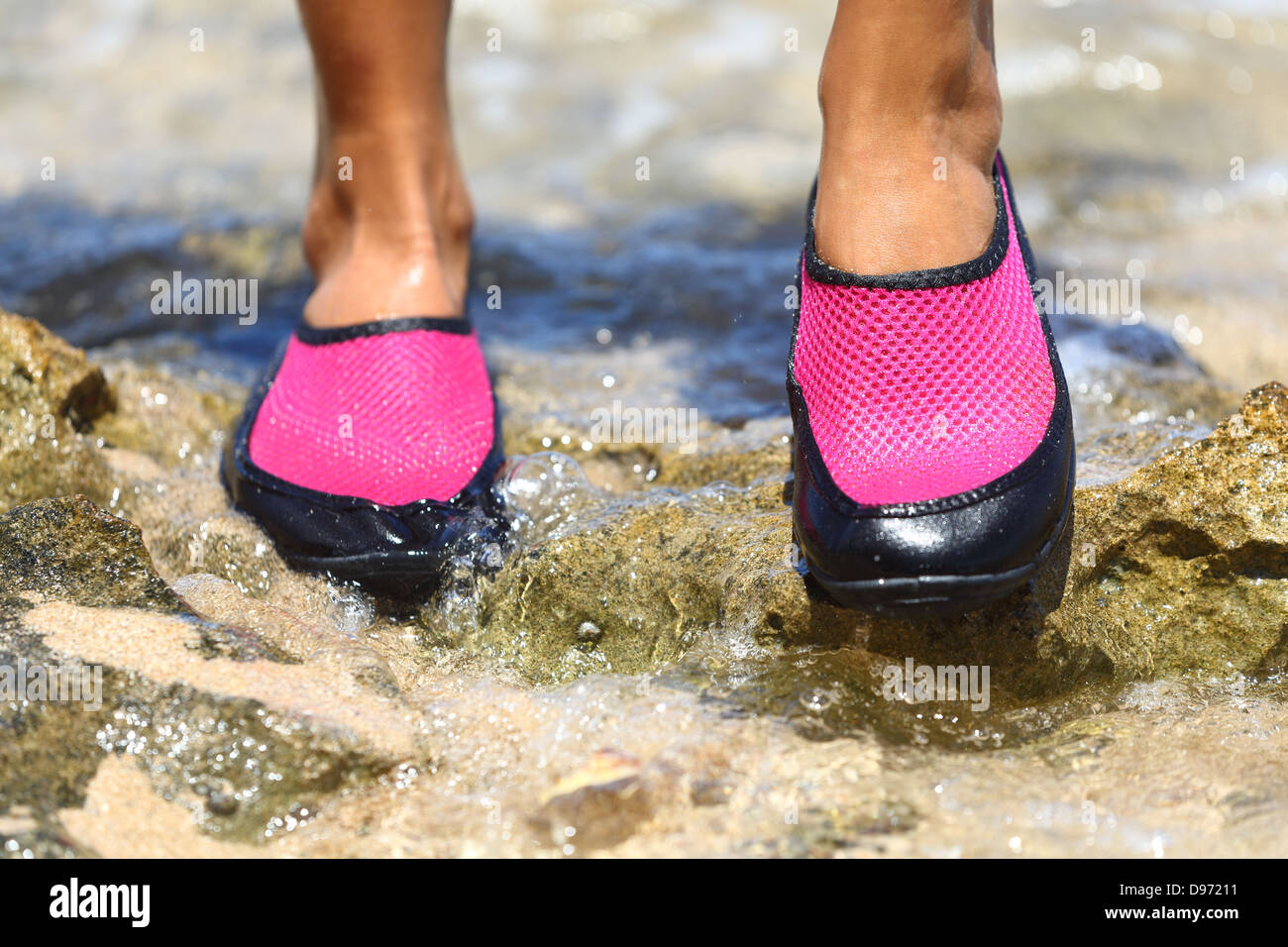 Zapatillas para el agua en neopreno rosa sobre las rocas en el agua en la playa. detalle de los pies una mujer vistiendo neopreno rosa brillante zapatos de agua