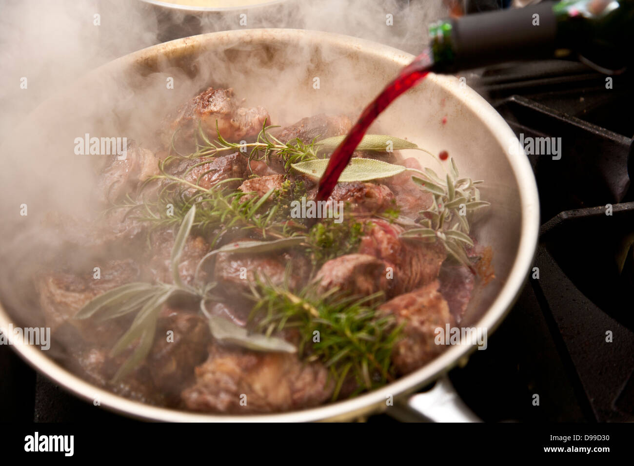 Estofado de Carne en una sartén con hierbas frescas y vino tinto. Foto de stock