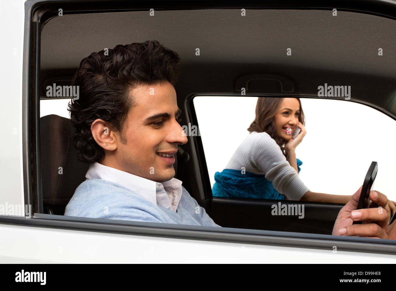 Hombre sentado en un automóvil con su novia hablando por teléfono móvil en segundo plano. Foto de stock