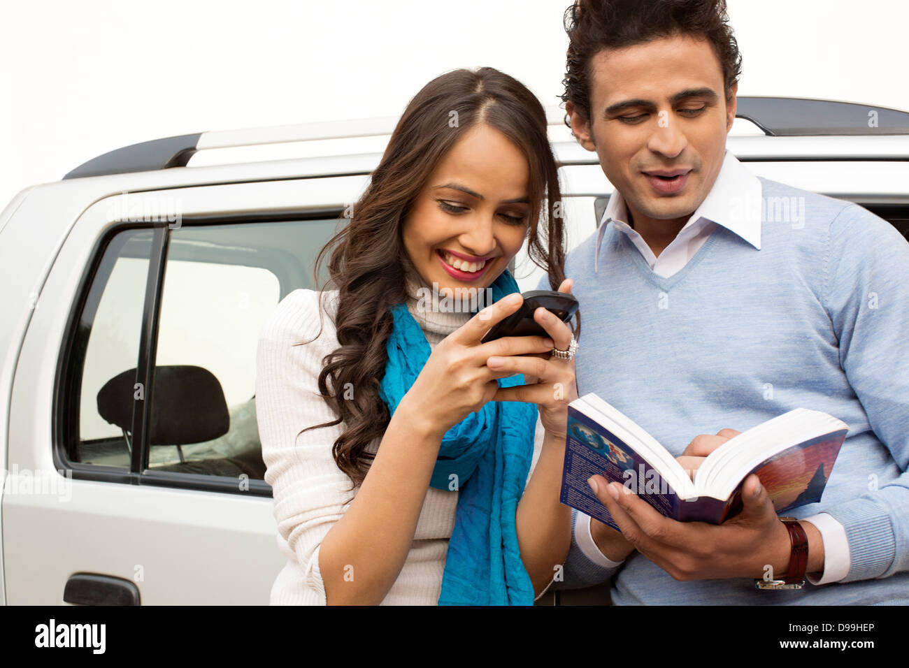 Mujer con mensajería de texto del teléfono móvil y un hombre leyendo un libro Foto de stock
