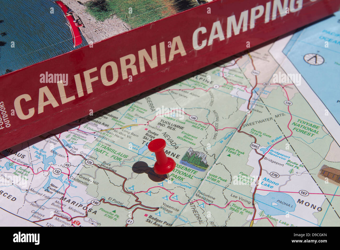Una chincheta marcando Yosemite National Park en un mapa de California junto a un libro de Camping California Foto de stock