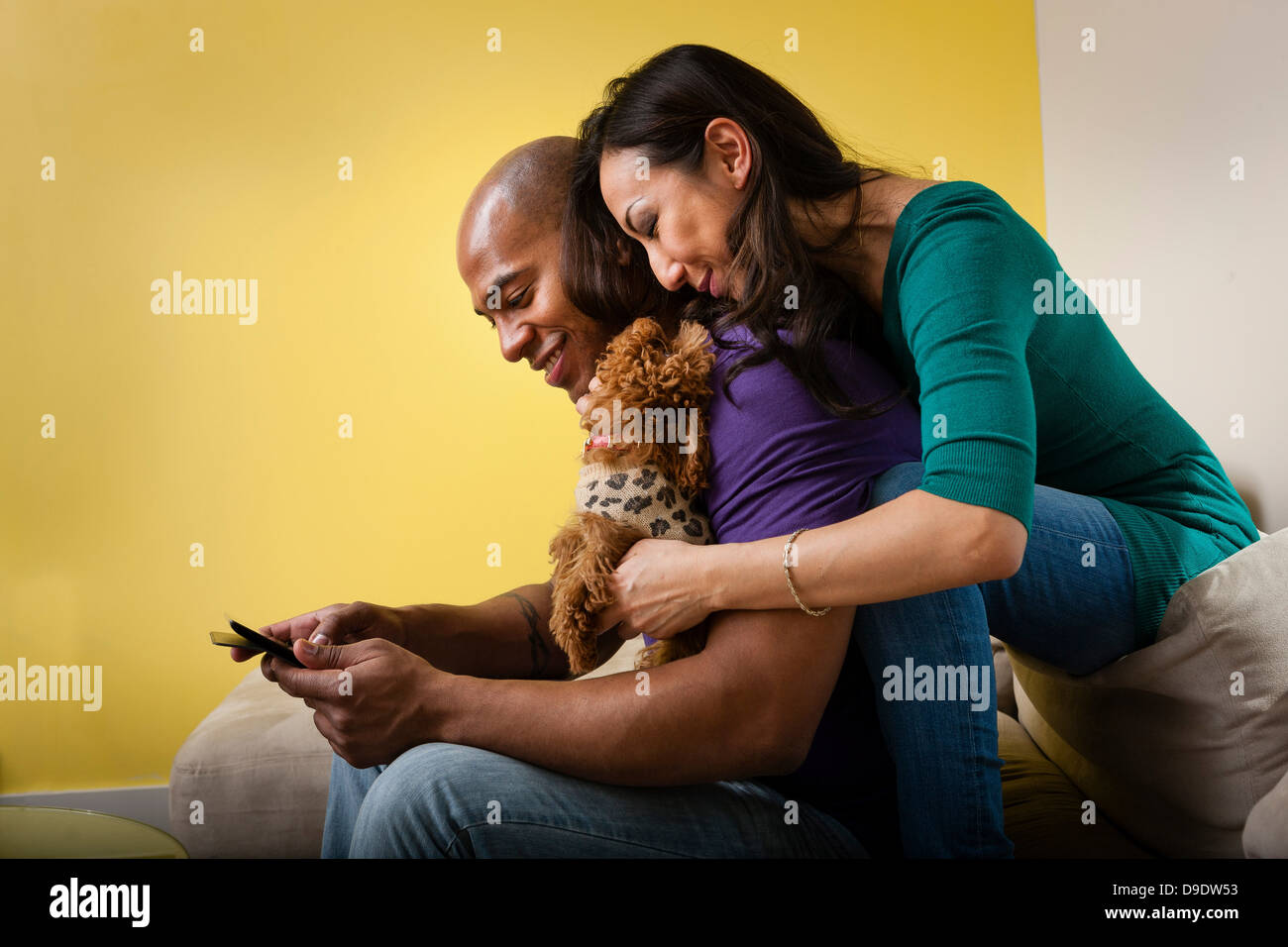 Adulto medio pareja sentada en un sofá con el perro y el smartphone Foto de stock