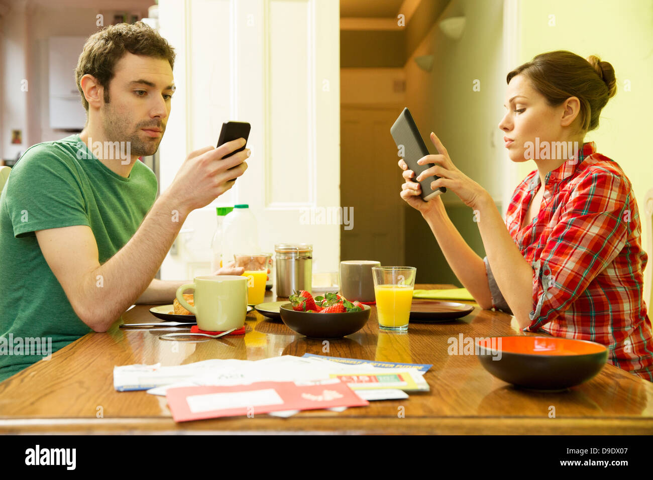 El hombre y la mujer mediante smartphone utilizando tablet digital en el desayuno Foto de stock