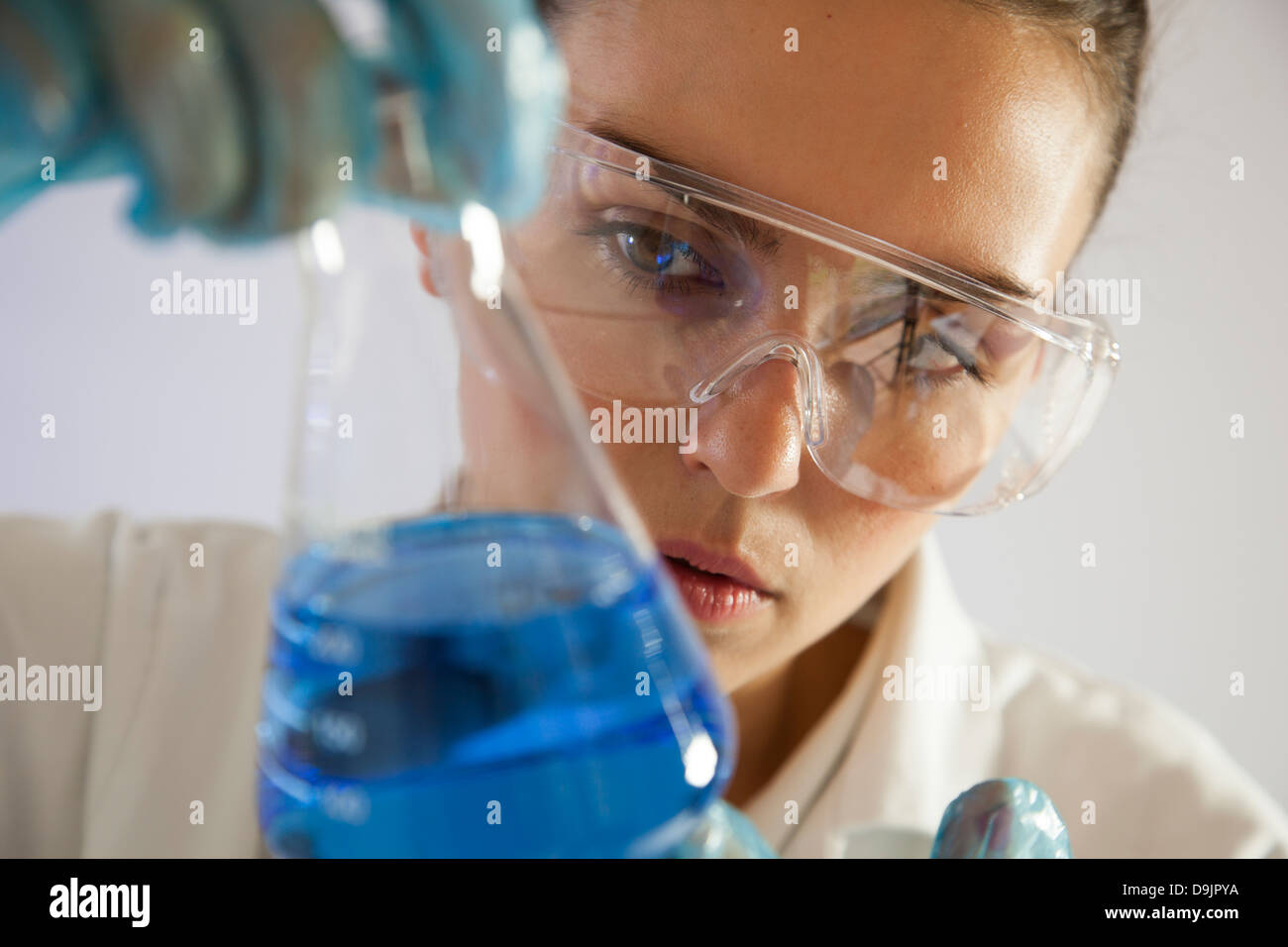 Técnico de laboratorio o científico femenino sosteniendo un vaso de precipitado de vidrio con líquido azul. Foto de stock