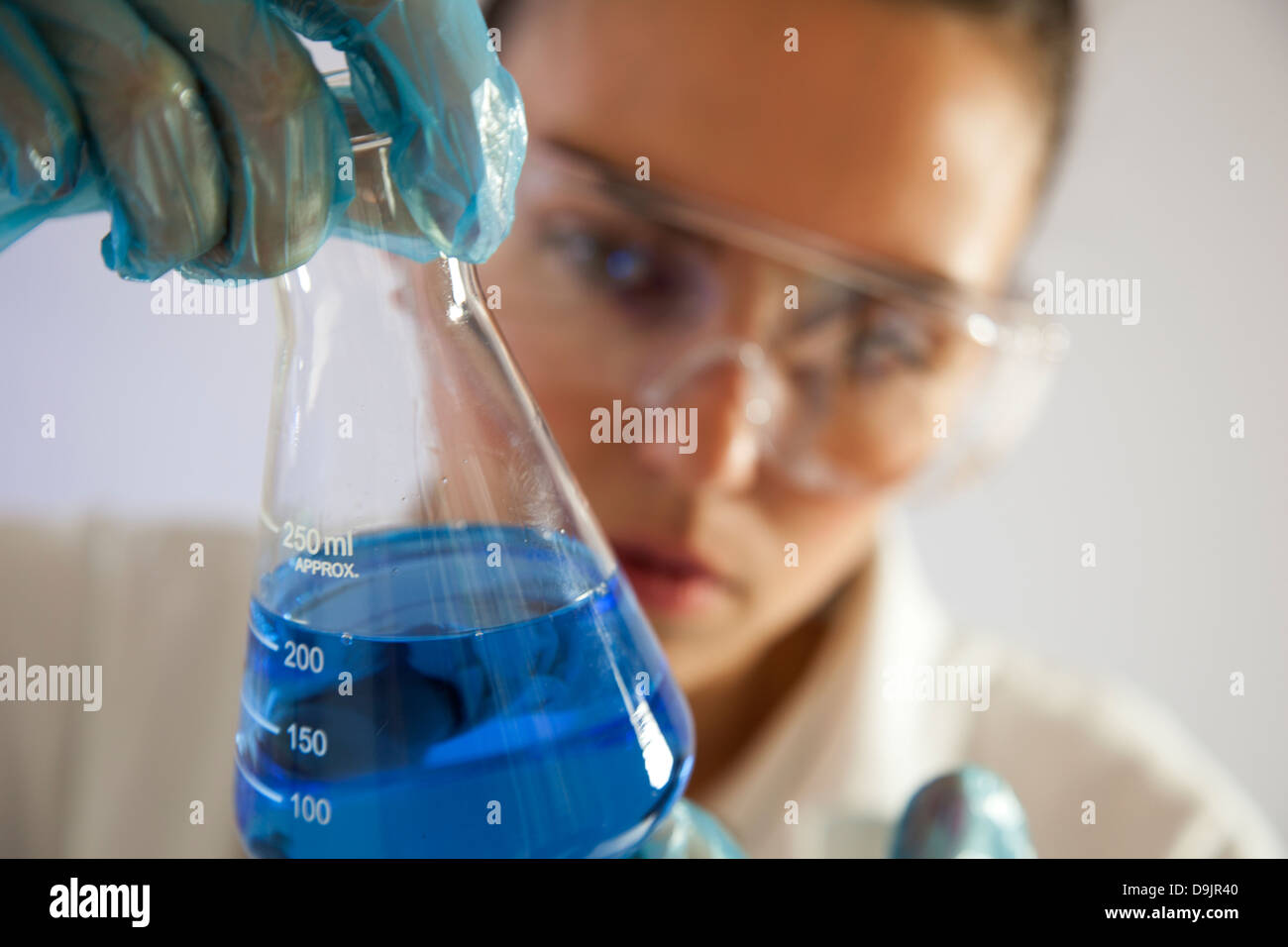 Técnico de laboratorio o científico femenino sosteniendo un vaso de precipitado de vidrio con líquido azul. Foto de stock