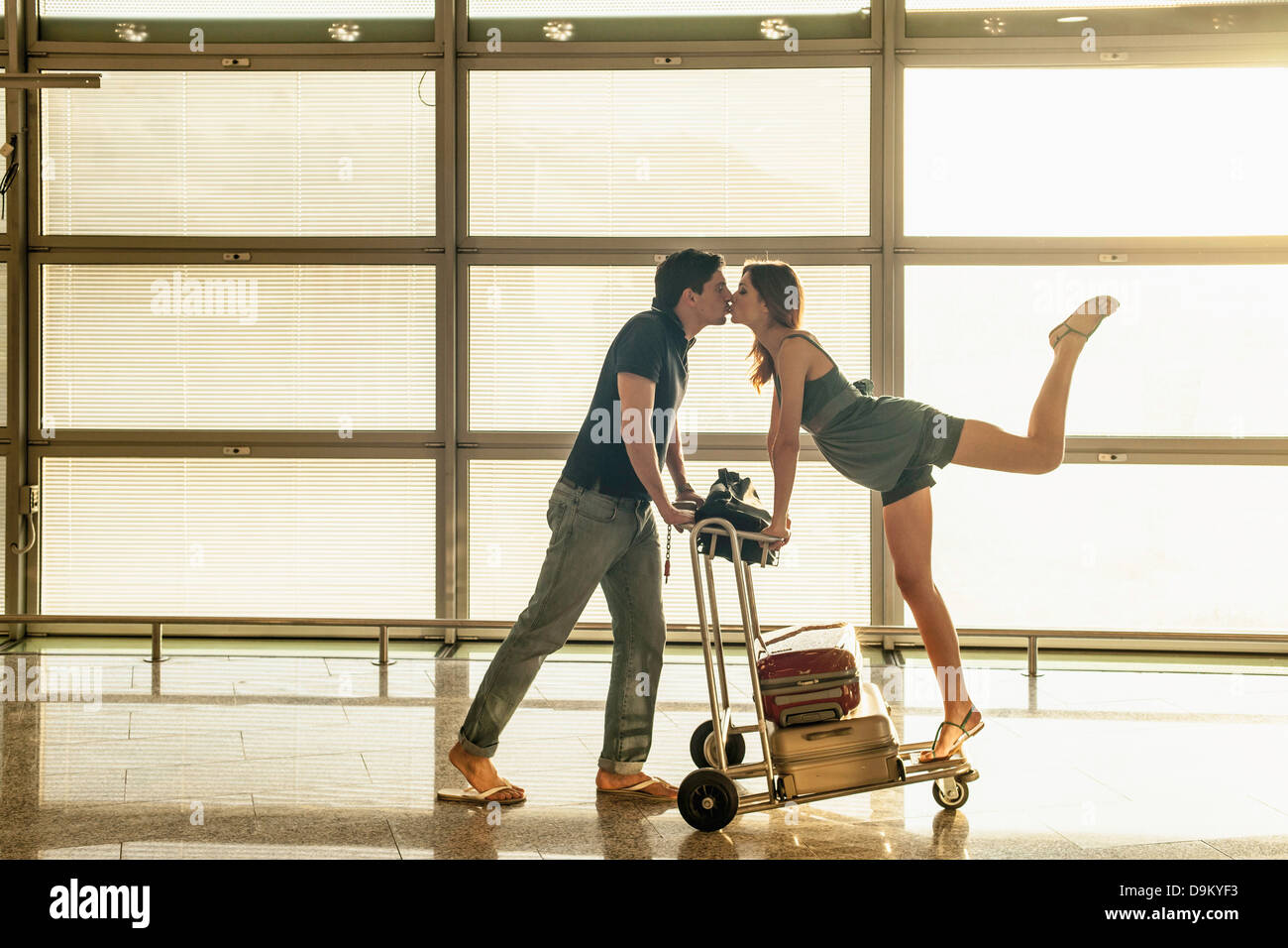 Pareja joven con carrito de equipaje en el aeropuerto besos Foto de stock