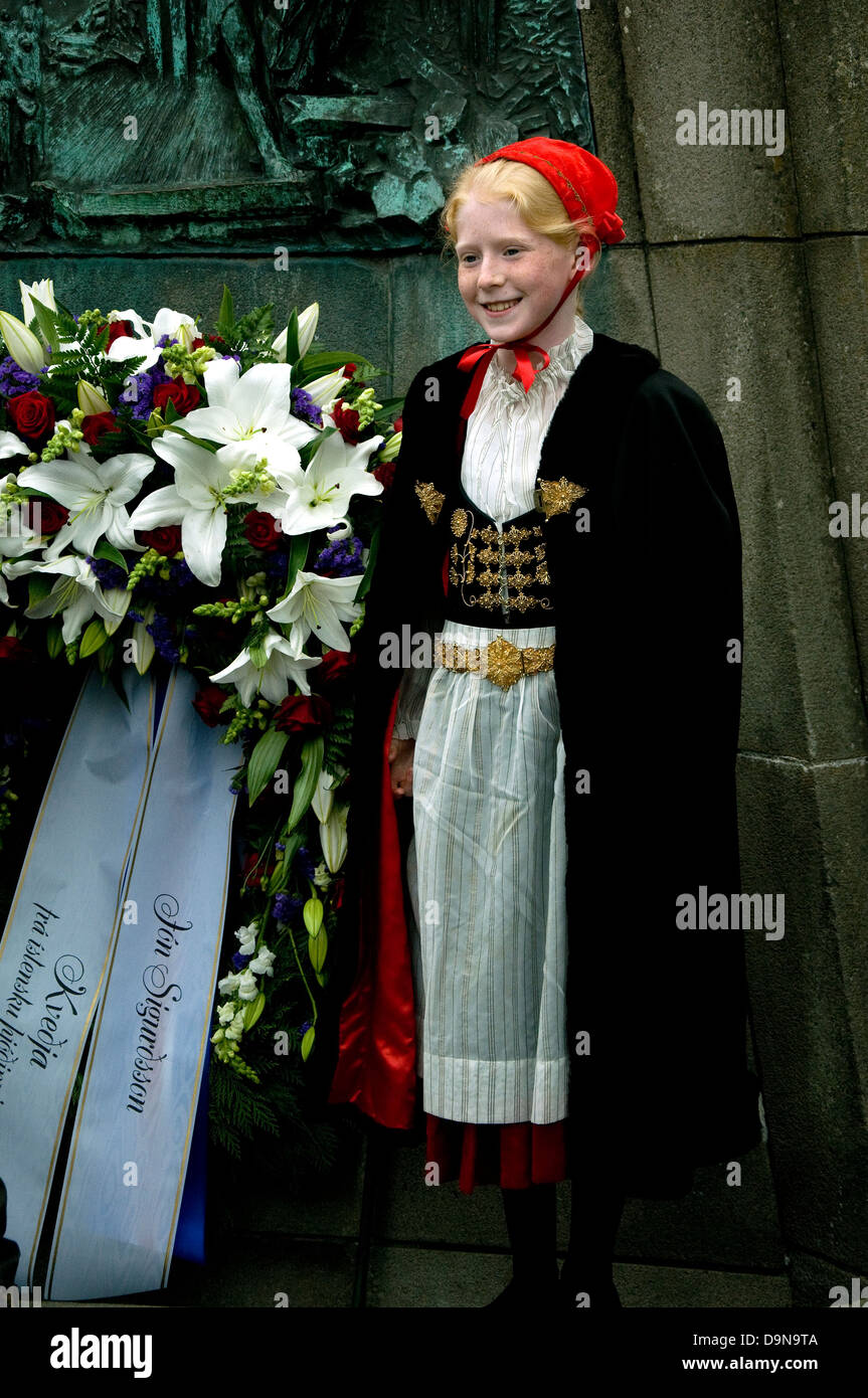 En Reykjavik, en el aniversario de la independencia de Islandia, una muchachita rubia posa en un memorial en el vestido nacional y vívida tapa roja Foto de stock