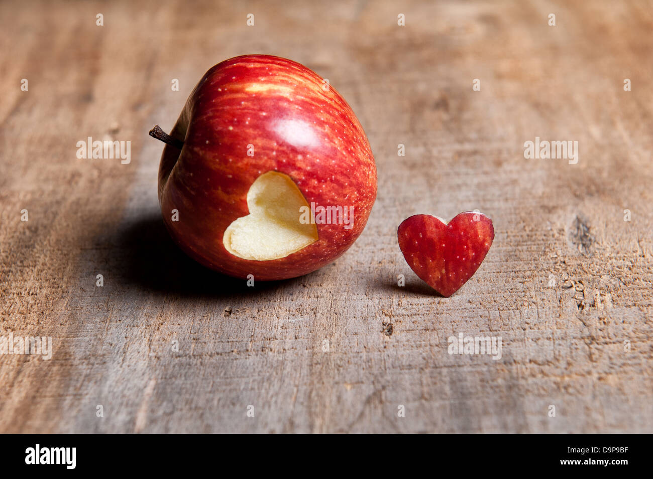 Manzana roja con forma de corazón cortado. El corazón de corte se coloca delante o al lado de la manzana en una superficie de madera de tonos cálidos. Amor Foto de stock