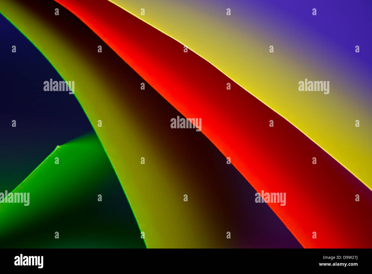 Macro y imagen abstracta de cartulina de color (rojo, amarillo y verde) con una forma curva sobre un fondo azul. Foto de stock