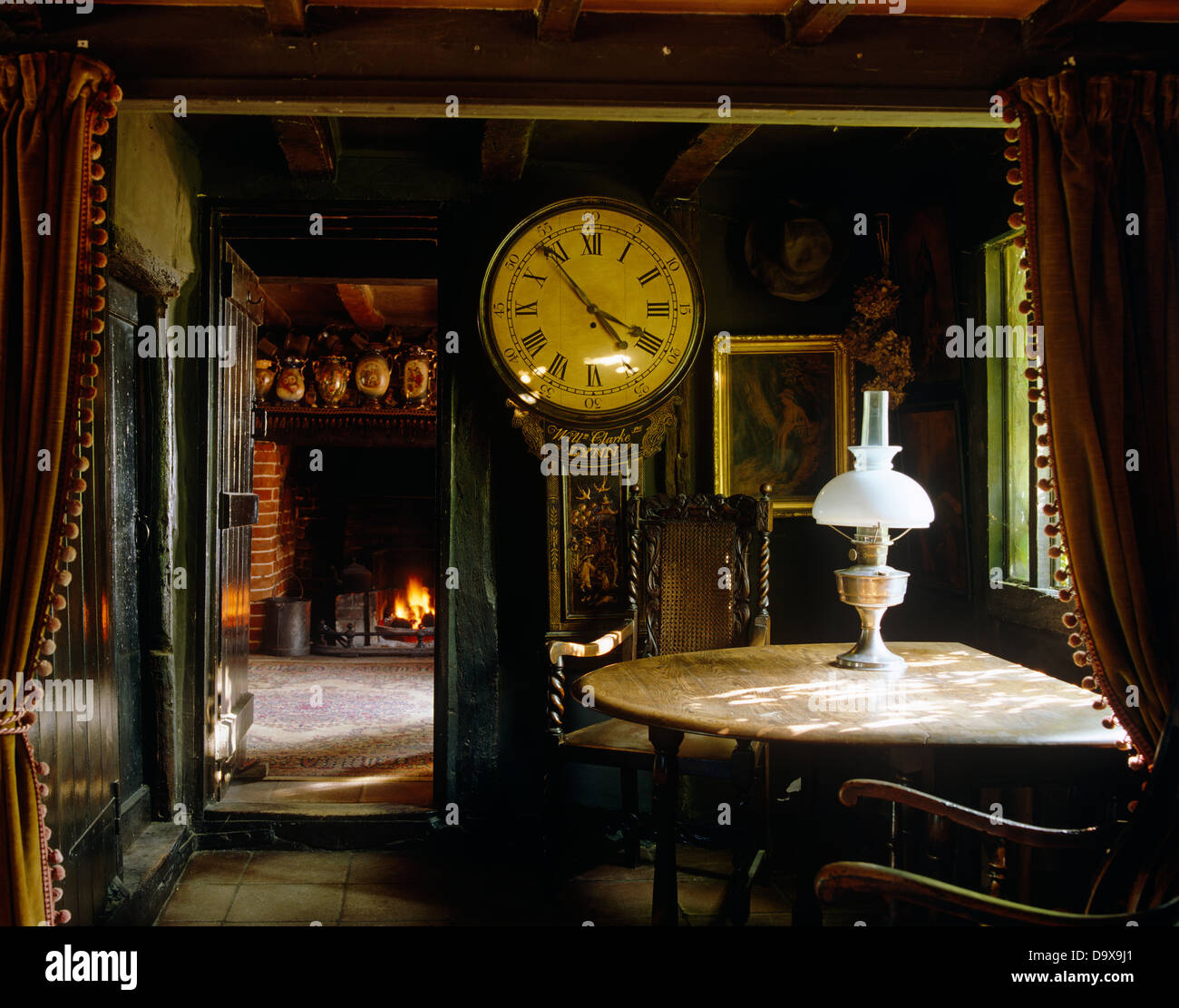 Antique mucho caso del reloj y mesa de madera antigua con lámpara de latón en Tudor cottage comedor con techo de vigas bajas Foto de stock