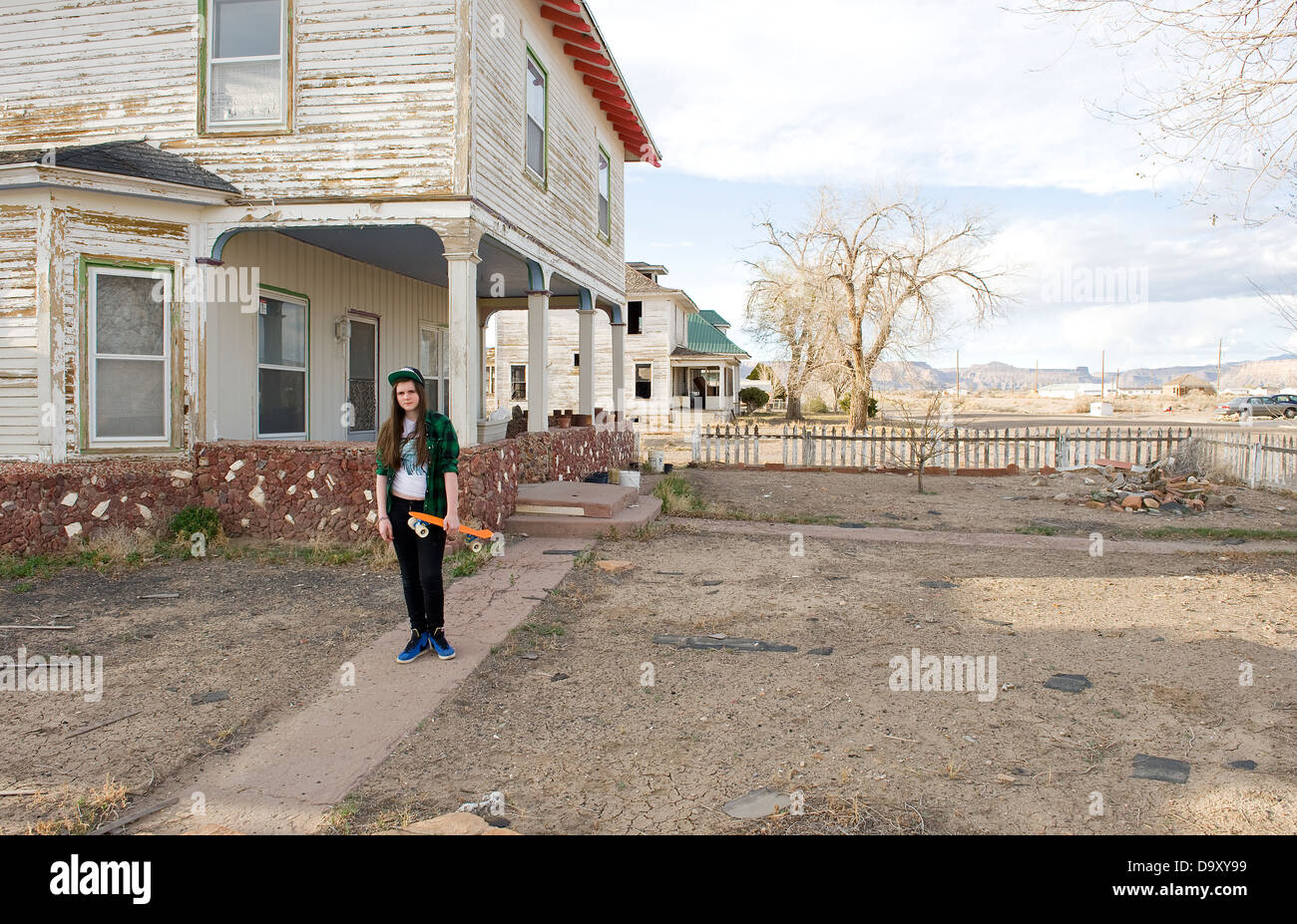 Adolescente con monopatín pie fuera de casa usando obedecer la tapa y comprobar verde camiseta, Green River, en Utah, EE.UU.. Foto de stock