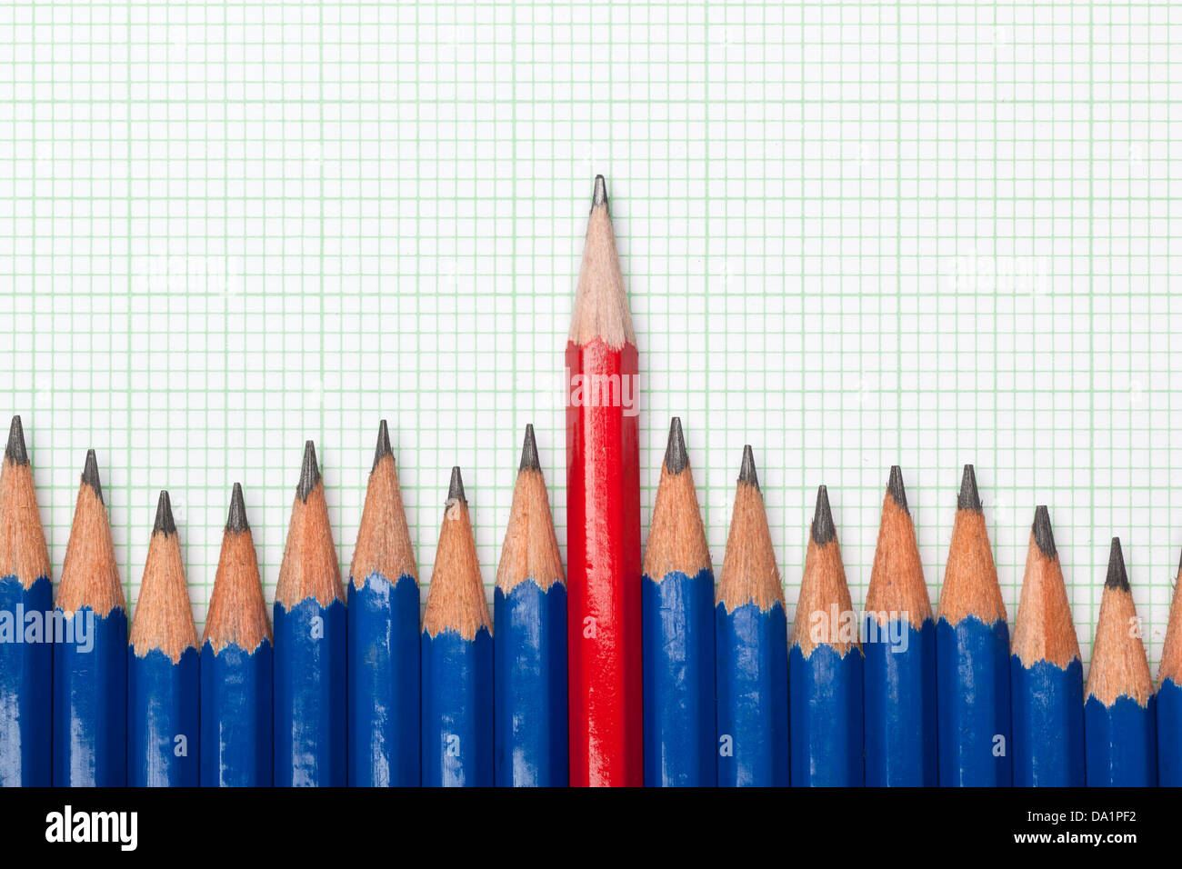 Lápiz rojo que sobresalían desde una fila de lápices de color azul sobre un trozo de papel milimetrado Foto de stock