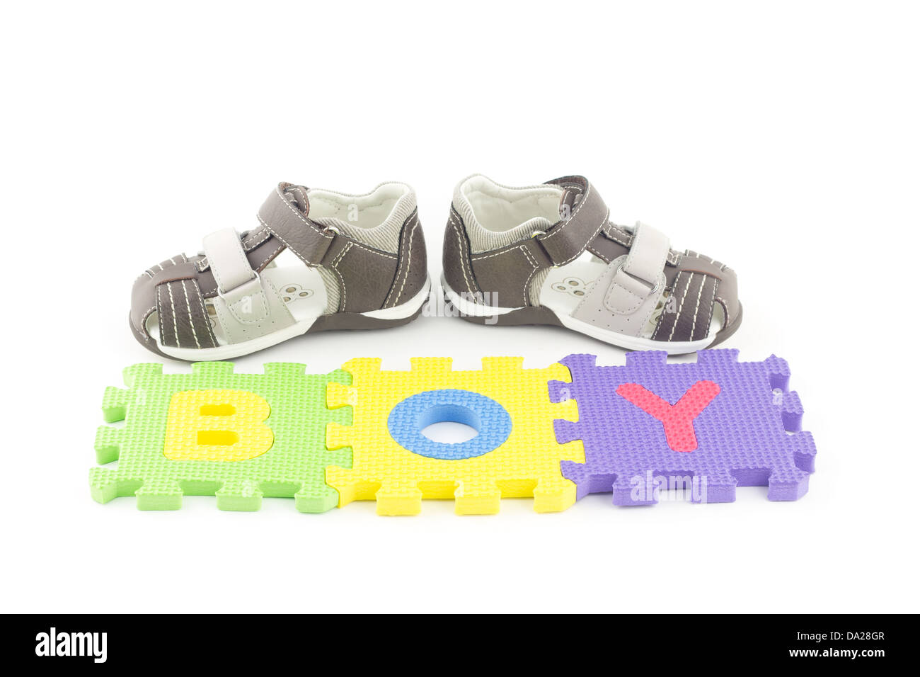 Sandalias de un niño delante de las piezas del rompecabezas del alfabeto aislado sobre fondo blanco. Foto de stock