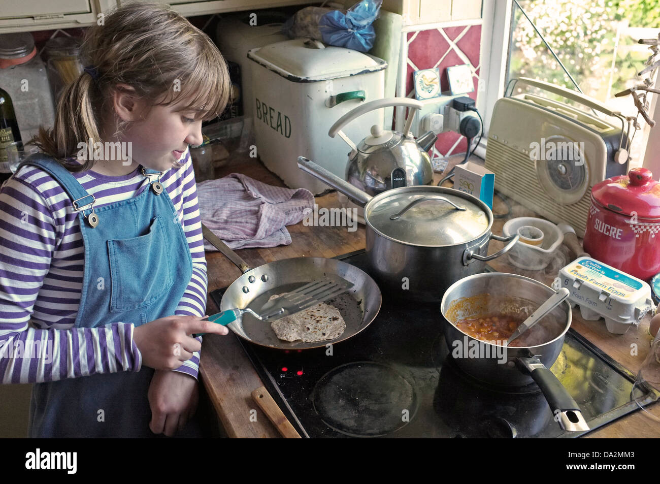 Una niña de 10 años aprendiendo a cocinar chapatis y garbanzos al curry. Foto de stock