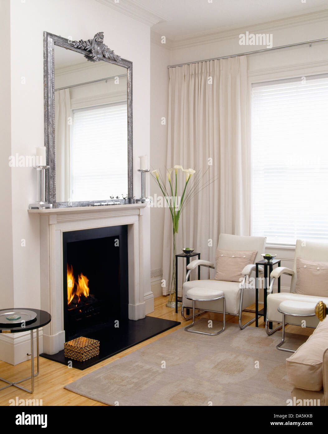 Par de sillones y taburetes y sofá frente a la chimenea en salón moderno  con alfombra gris y ventanas con cortinas blancas Fotografía de stock -  Alamy