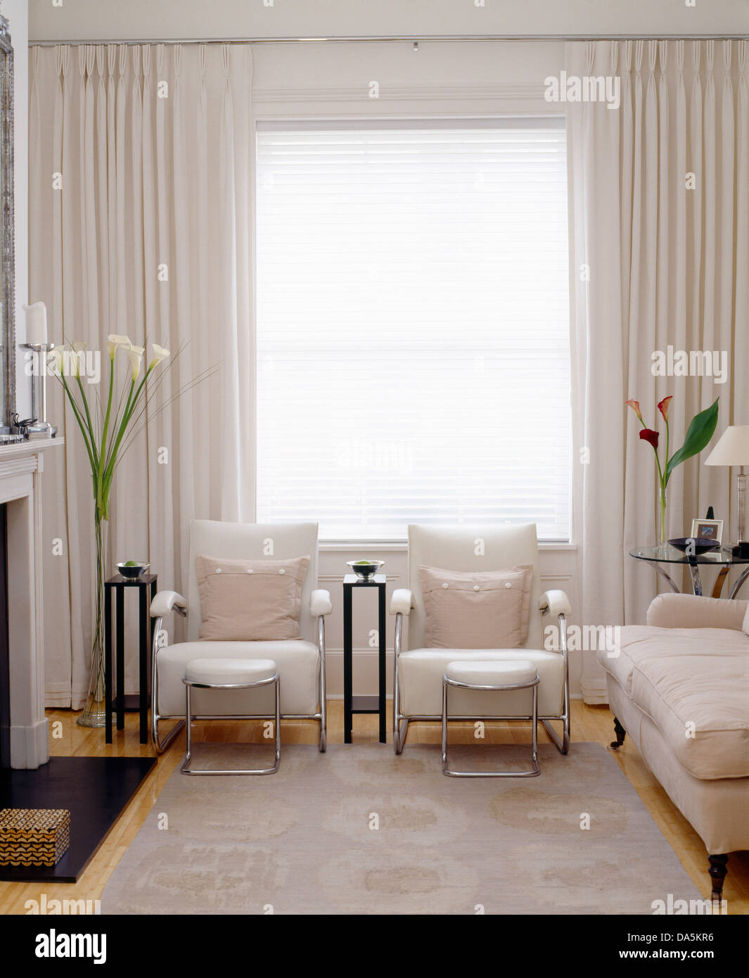 Par de sillones y taburetes y sofá frente a la chimenea en salón moderno  con alfombra gris y ventanas con cortinas blancas Fotografía de stock -  Alamy